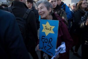 Naomi Wimborne-Idrissi, of Jewish Voice for Labour holds up a sign at the #EnoughIsEnough Demonstration against antixemitism, featuring a yellow star and the word Jews Photo Credit: Marc Morris