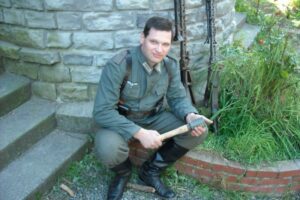 Younger Mishin wearing a World War II-era German uniform featuring a swastika and holding a hand grenade. Twitter